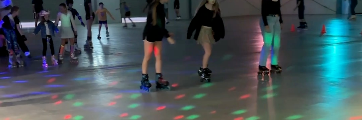 People roller skating in an indoor rink with colorful lights on the floor.