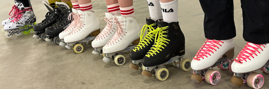 Roller skates with various colors and designs worn by people on a wooden floor.